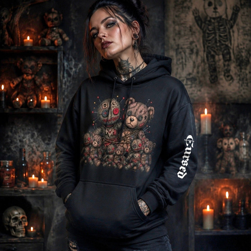 A woman modeling a black hoodie with a teddy bear graphic print and 'Cursed' written on the sleeve, set against a dark, gothic room with candles and skulls.