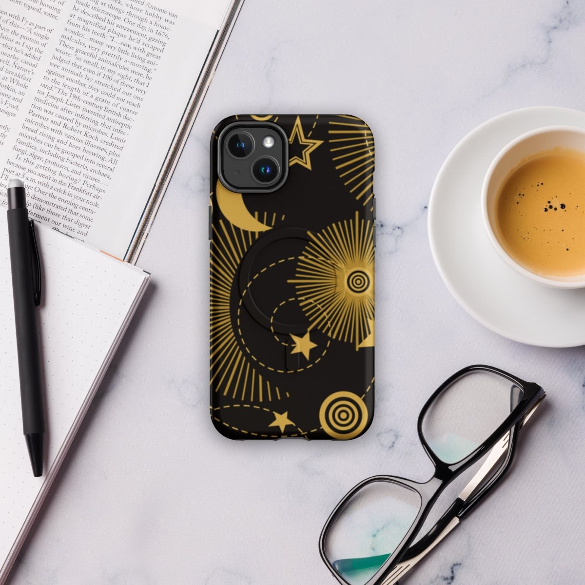 Phone case with celestial design on a marble surface with a cup of coffee, glasses, and pen.