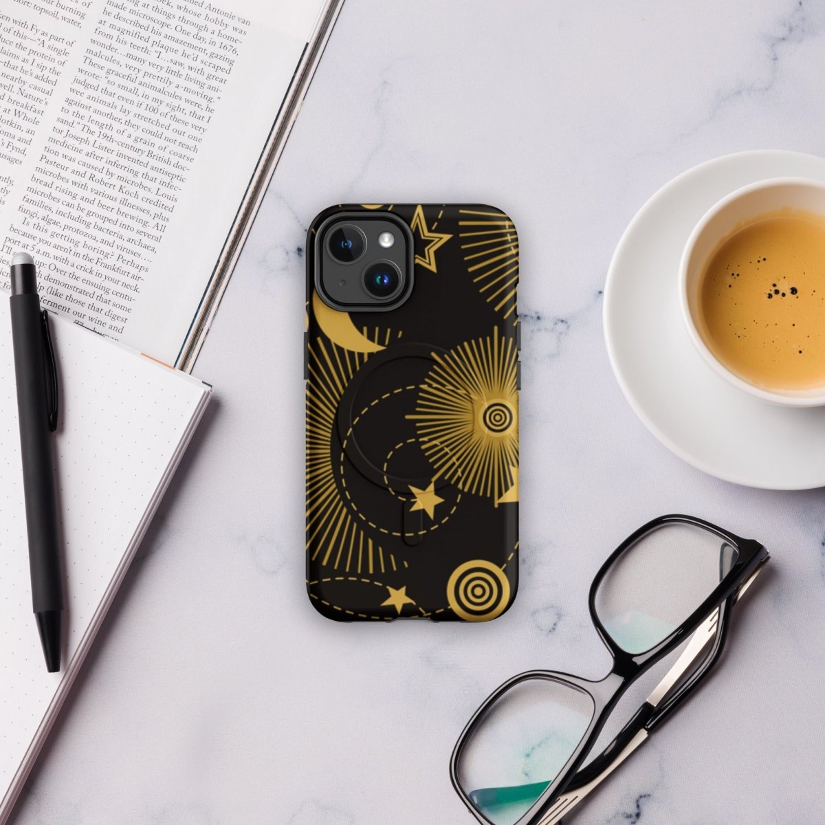 Phone case with celestial design on a marble surface with a book, pen, and coffee.