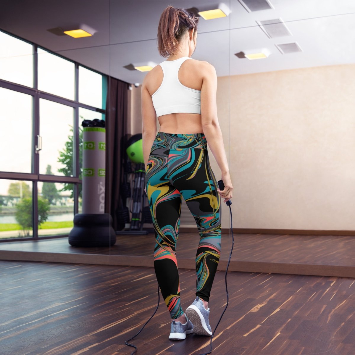 Woman in colorful leggings and white sports bra holding a jump rope in a gym.